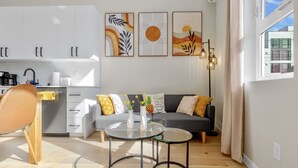 Una cocina moderna con armarios blancos, una mesa de comedor con sillas y un sofá con cojines. Hay tres obras de arte enmarcadas en la pared sobre el sofá.