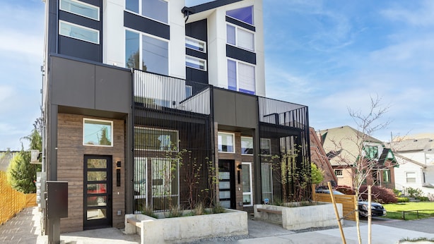 Un edificio residencial moderno de varios pisos con una combinación de paneles exteriores oscuros y claros, ventanas amplias y una entrada con portón.