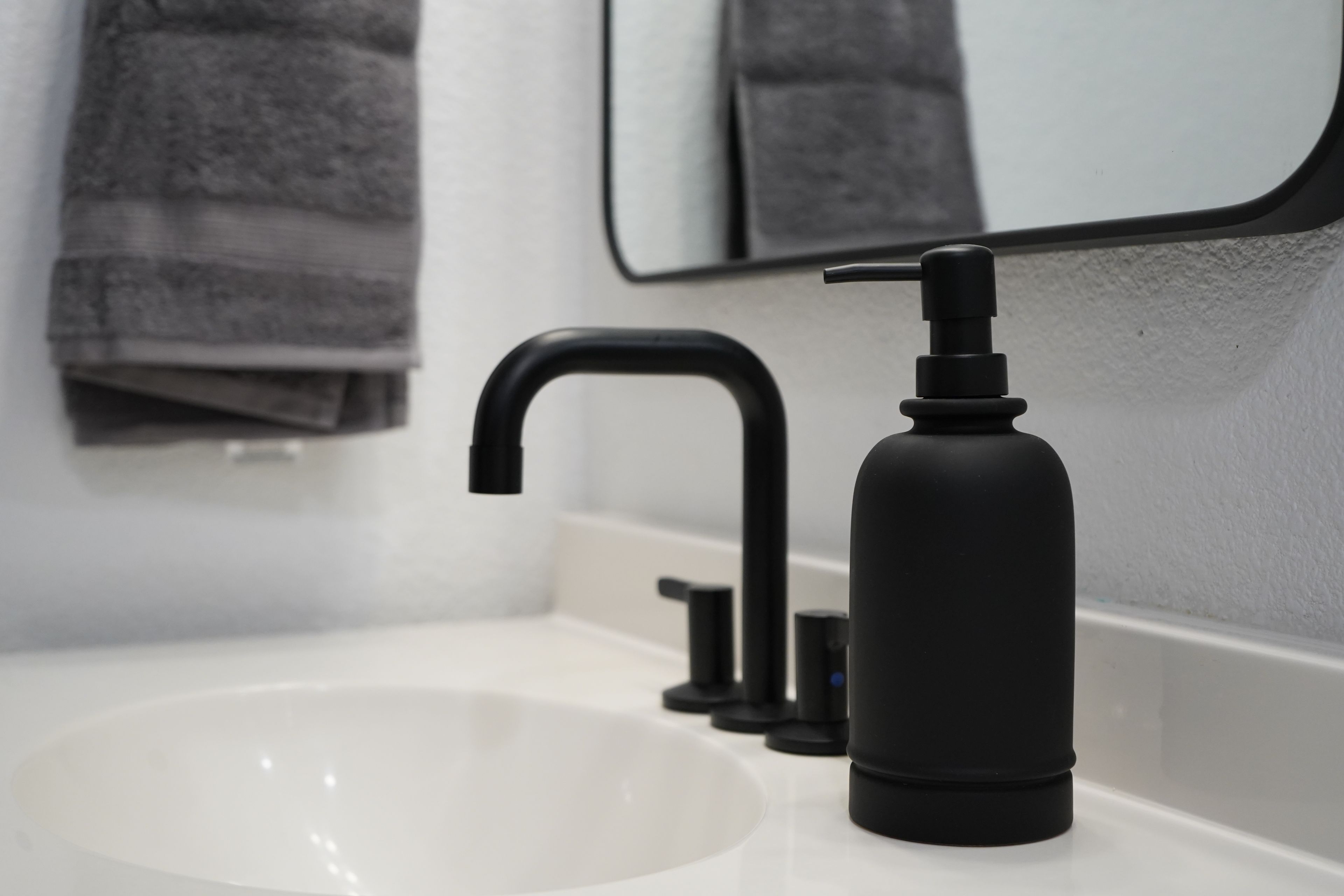 Une salle de bain moderne avec un lavabo blanc, un robinet noir et un distributeur de savon noir.