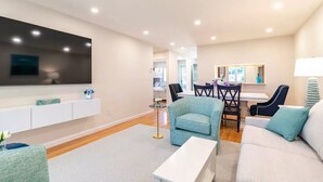 A modern living room with a flat-screen TV, a dining area with a table and chairs, and a sofa. - Ocean Edge Cape Cod 2 Bed 2 Bath, Golf & Free Resort Access - Brewster, MA (Brewster)