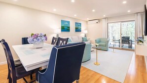 A modern living room with a dining area, a sofa, a chair, and a table with a vase of flowers. - Ocean Edge Cape Cod 2 Bed 2 Bath, Golf & Free Resort Access - Brewster, MA (Brewster)