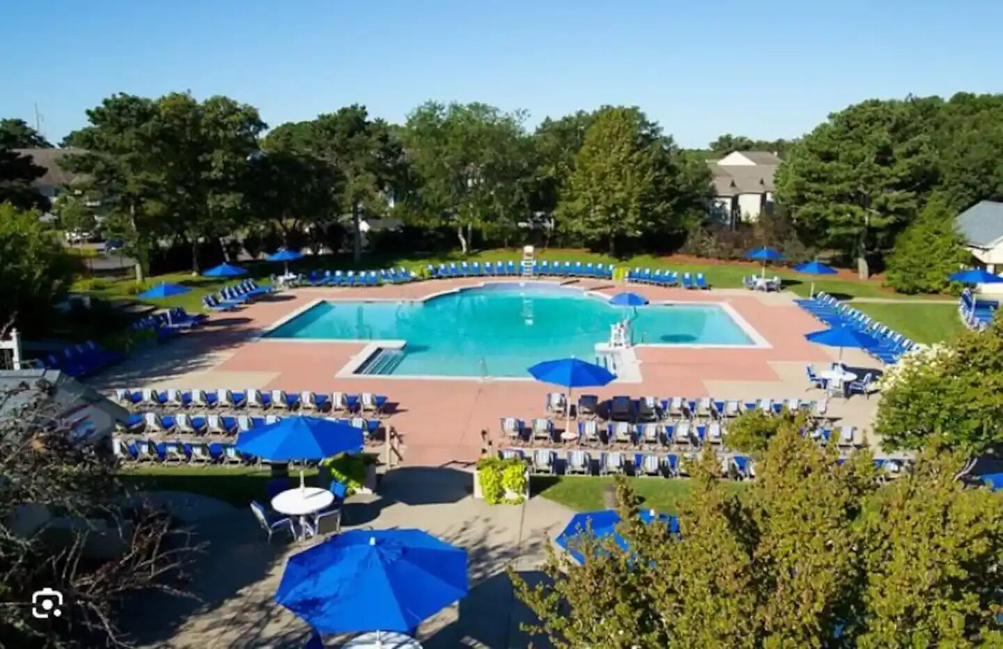 A large outdoor swimming pool surrounded by lounge chairs and umbrellas, with a clear sky above.