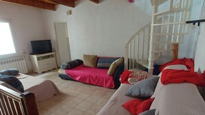 A cozy living room with a sofa, a television, and a staircase. - Maison de Village (Puimisson)