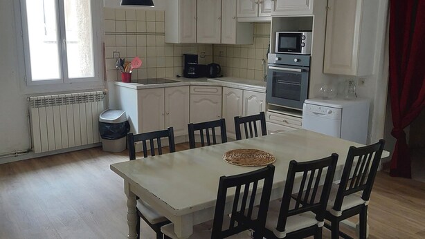 A compact kitchen with white cabinets, a central island with chairs, a microwave, oven, and a coffee maker. - Maison de Village (Puimisson)