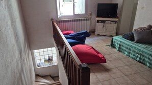 A room with a staircase, a radiator, a television on a stand, and a bed with pillows. - Maison de Village (Puimisson)