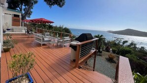 Une terrasse en bois avec des meubles d’extérieur, un barbecue et un parasol rouge.