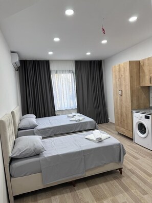 Ein modernes Schlafzimmer mit zwei Betten, einer Waschmaschine und einem großen Fenster mit Vorhängen.