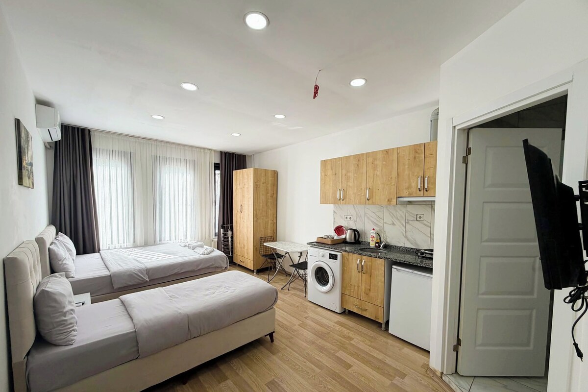 A compact living space with a sofa bed, a washing machine, and a small kitchen area.