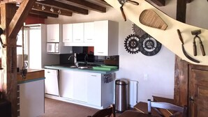 A kitchen with white cabinets, a microwave, and a sink. There are wooden beams on the ceiling and a trash can near the sink. - Le Vernay - Pierreclos (PIERRECLOS)