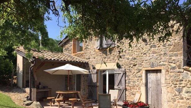 A stone building with a patio area featuring a table and chairs, a wooden swing, and a wheelbarrow with flowers. - Le Vernay - Pierreclos (PIERRECLOS)