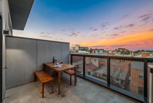 Relax on the balcony with a view of the cityscape, featuring a table and bench for dining or unwinding.