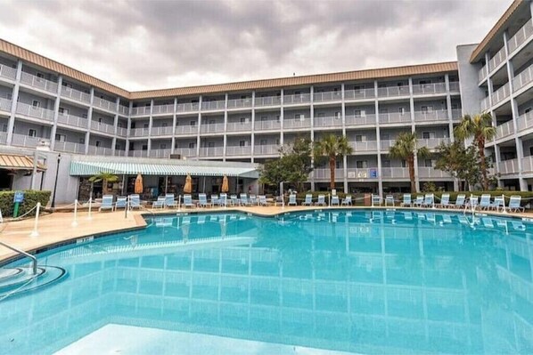 A hotel with a large swimming pool, multiple balconies, and a covered seating area.