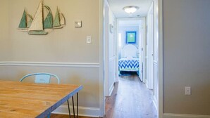 Un couloir avec une table et des chaises en bois, une porte donnant sur une chambre à coucher avec un lit et une couvre-lit à motifs bleus et blancs.