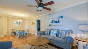 Un salon doté d’un ventilateur de plafond, d’un canapé, d’une table basse et d’un coin repas avec des chaises et une table.