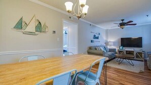 Un coin repas avec une table en bois et des chaises bleues, un canapé, un téléviseur et un ventilateur de plafond.