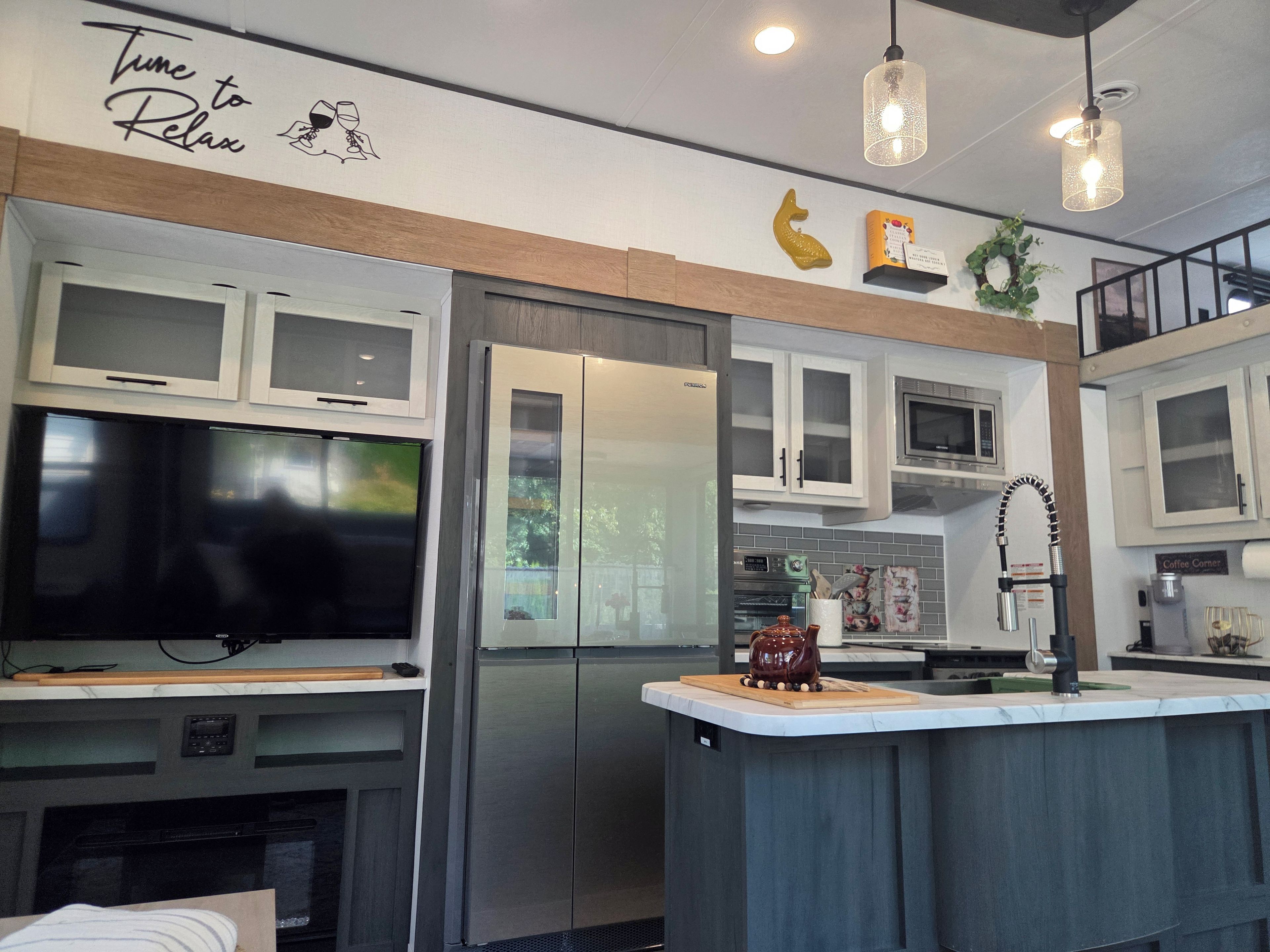 Una cocina moderna con refrigerador, microondas y horno integrados. Hay un televisor de pantalla plana grande montado sobre la encimera.