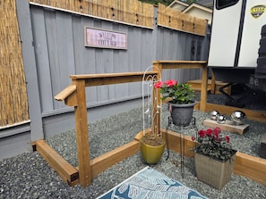 A wooden bench with a hanging plant, a welcome sign, and a small table with decorative spheres.