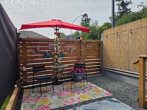 A patio with a table and chairs, a red umbrella, and a decorative fence.