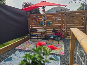 A patio area with a wooden fence, two chairs, a table, and a red umbrella.