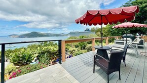 A deck with outdoor seating, a view of the sea, and a cruise ship in the distance. - A Private Space by Villa Sunbeam. (St. Thomas)