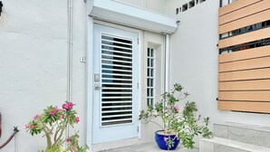 A white door with horizontal blinds, a blue potted plant with pink flowers, and a wooden slat wall. - A Private Space by Villa Sunbeam. (St. Thomas)