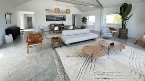 Un vaste espace de vie doté d’un haut plafond, d’un canapé blanc, d’une table basse et d’un coin repas avec des chaises et une table.