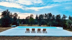 Un espace piscine extérieur moderne, doté de quatre chaises longues en bois et d’une terrasse blanche.