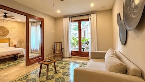 Habitación de hotel con cama, sofá, mesita, silla, ventilador de techo y vistas al exterior a través de una puerta de vidrio.