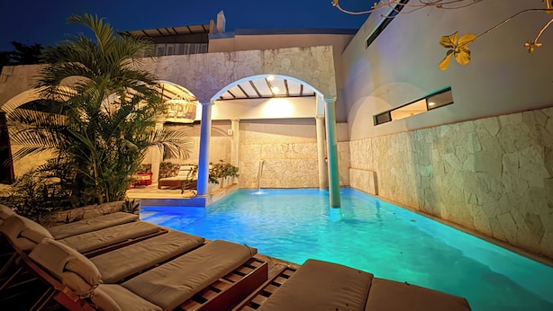 Una piscina interior con sillas de descanso, un muro de piedra y un ventilador de techo.