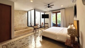 Un dormitorio espacioso con una cama grande, una zona de estar con sillas, una bañera y un balcón con cortinas.