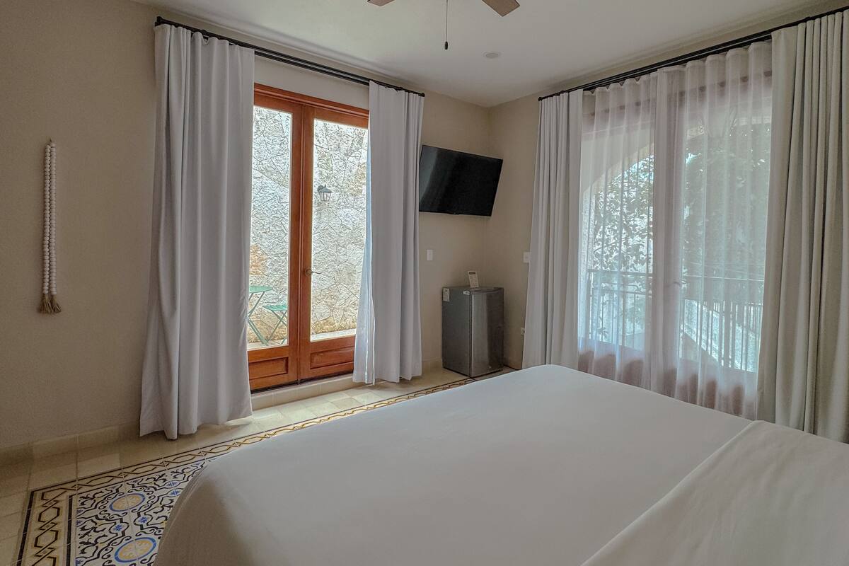 A bedroom with a large bed, a ceiling fan, a TV mounted on the wall, and a view of the outdoors through a glass door.