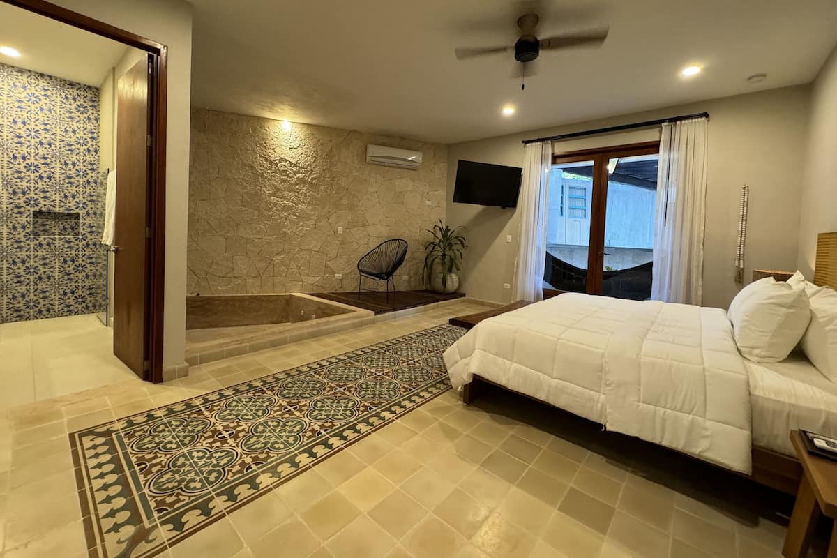 A bedroom with a large bed, a bathtub, a chair, and a TV.