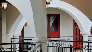 Un pasillo interior con arcos blancos, barandillas negras y puertas rojas.