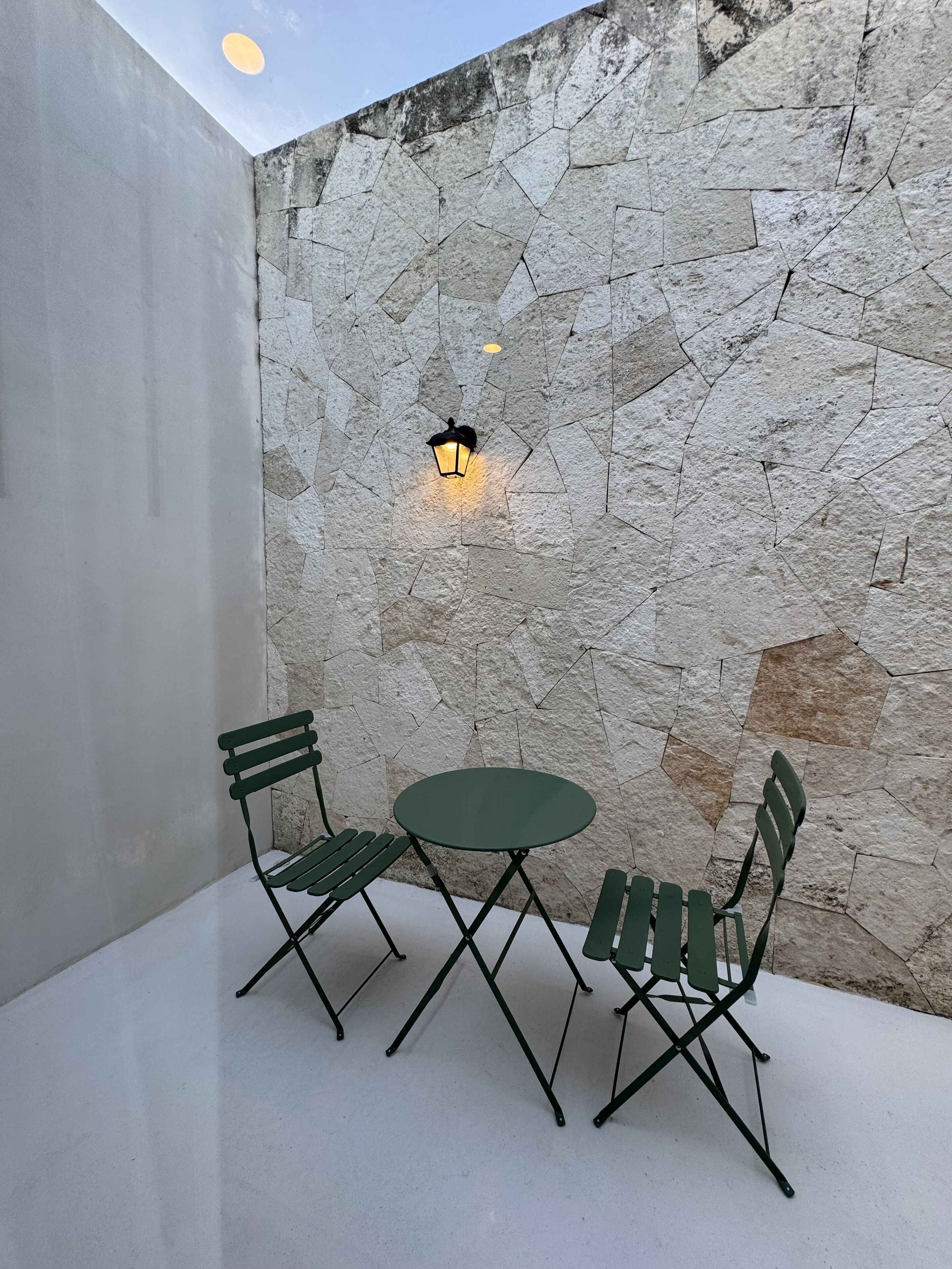 Un petit espace extérieur aménagé avec un mur en pierre, une table ronde et deux chaises.