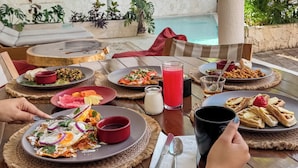 Un comedor con mesas, platos de comida y una piscina al fondo.