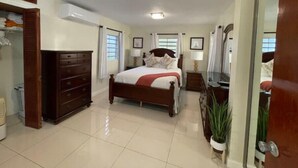 A well-lit bedroom with a large bed, a dresser, a mirror, and a potted plant. - Angie's Sunset View (St Thomas)