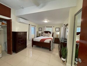 Ein helles Schlafzimmer mit einem großen Bett, einem Schminktisch, einem Spiegel und einer Topfpflanze.