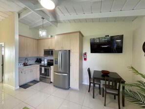 Eine moderne Küche mit Edelstahlgeräten, ein Essbereich mit Tisch und Stühlen sowie ein an der Wand befestigter Flachbildfernseher.