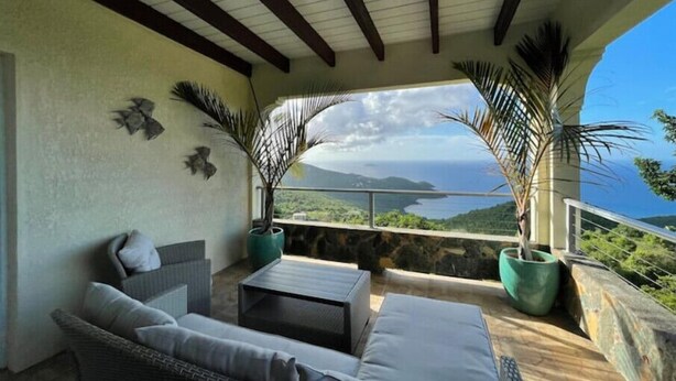 A cozy seating area with a view of a coastal landscape. - Angie's Sunset View (St Thomas)