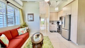 A modern living room with a red sofa, a glass coffee table, and a kitchen area with stainless steel appliances. - Angie's Sunset View (St Thomas)