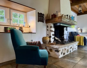 A cozy living room with a teal armchair, a fireplace, and a window overlooking greenery.