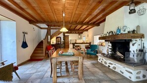 A rustic interior with a wooden dining table, chairs, a fireplace, and a staircase leading to another room. - Artegia - Sainte-engrace (SAINTE-ENGRACE)