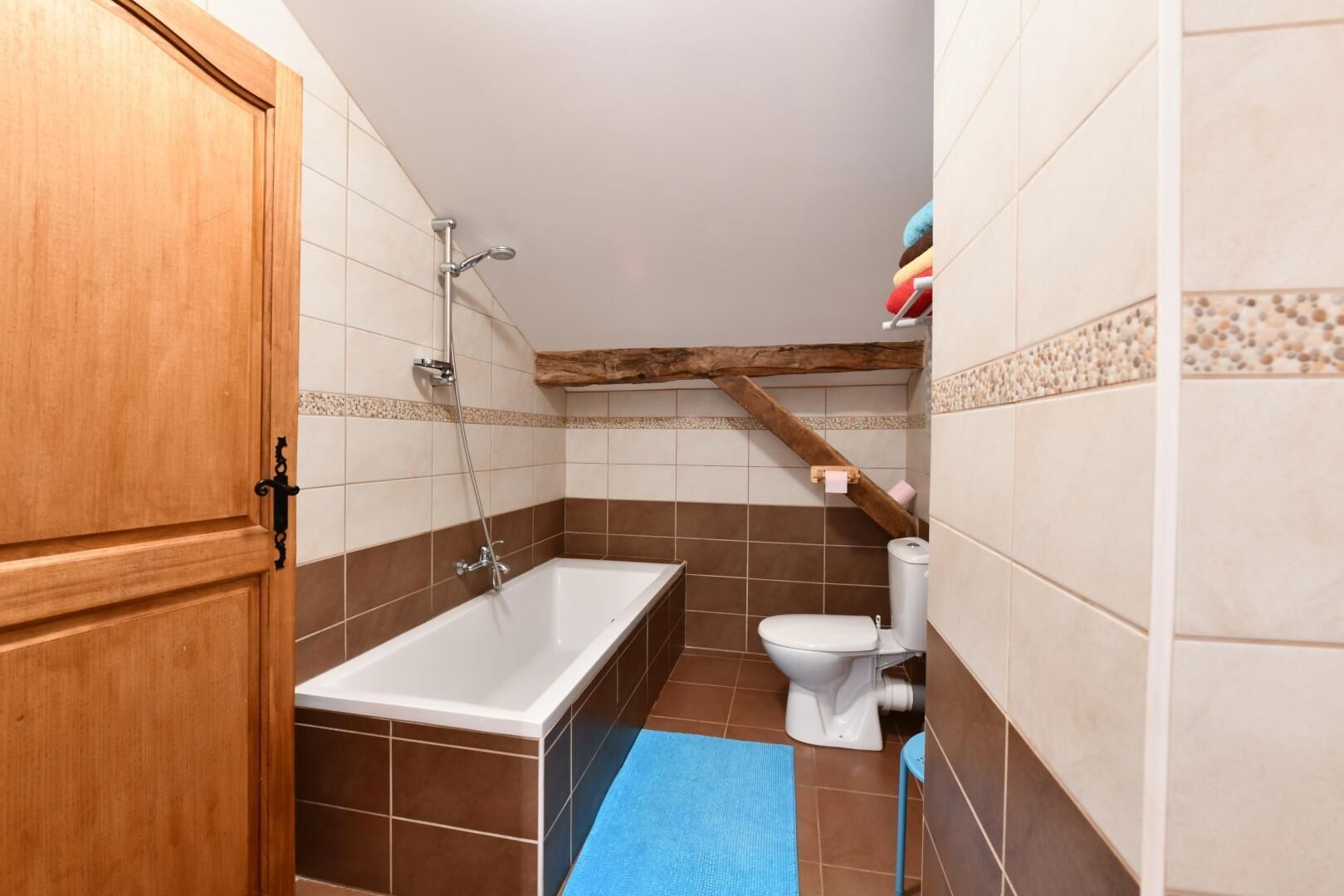 A bathroom with a bathtub, toilet, and wooden ceiling beams.