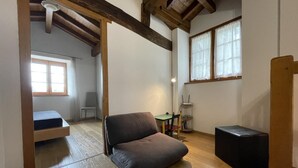 Een compacte kamer met een houten plafond, een bank, een klein tafeltje en een stoel.