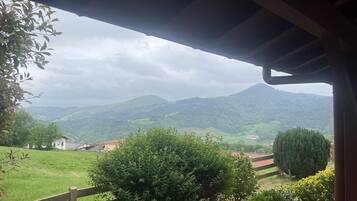 Une vue depuis un espace extérieur abrité, avec une clôture en bois, de la verdure et des collines au loin.