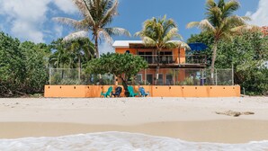 A beach with a fenced area, a building with a balcony, and palm trees.