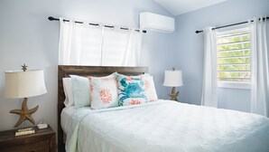 A bedroom with a bed, two bedside tables, a nightstand, a window with curtains, and an air conditioning unit on the wall.