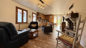 A cozy living room with a fireplace, a dining area, and a kitchen with wooden cabinets. - Aguerrea - Macaye - Gîte (MACAYE)