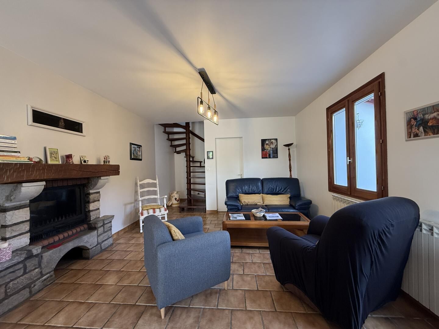 Una sala de estar con chimenea, un sofá azul, una mesa de centro de madera y una escalera que lleva a otra habitación.