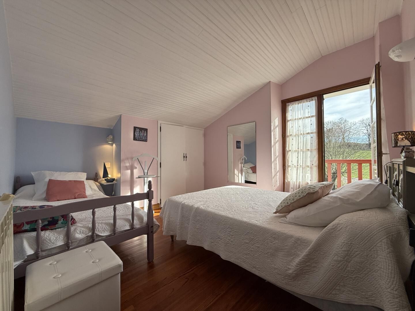 A bedroom with a wooden bed, a bench, a desk, and a window with a view of trees.